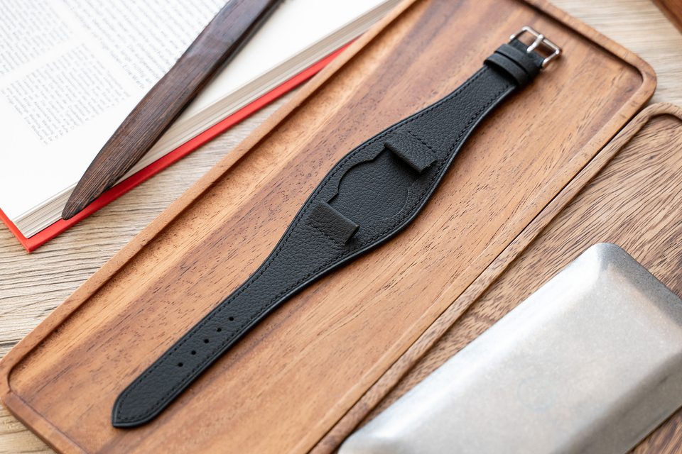 Black pebbled Bund strap laid flat on a wooden tray.