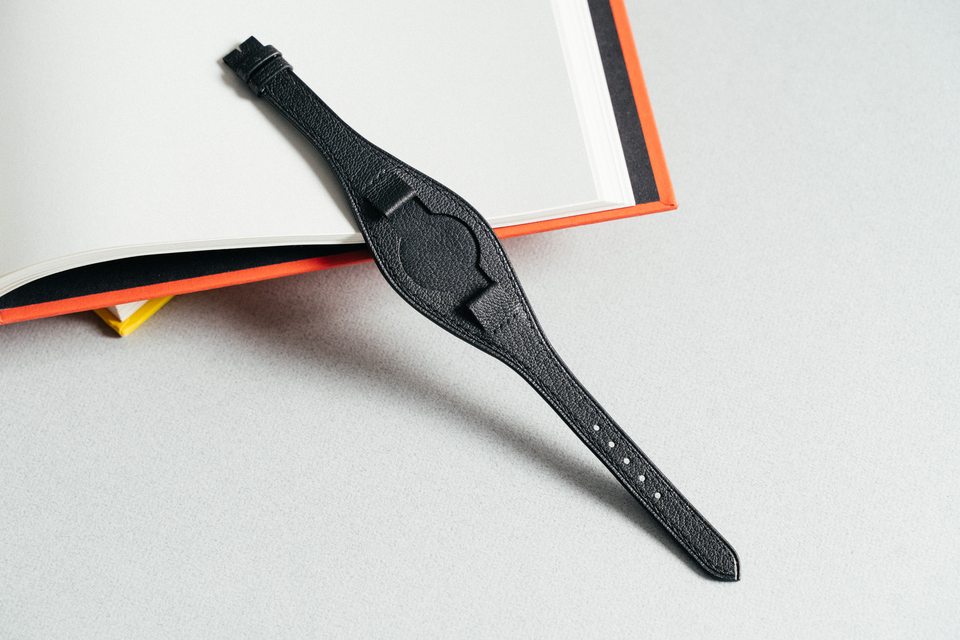 Full black pebbled Bund strap beside the corner of an open book.