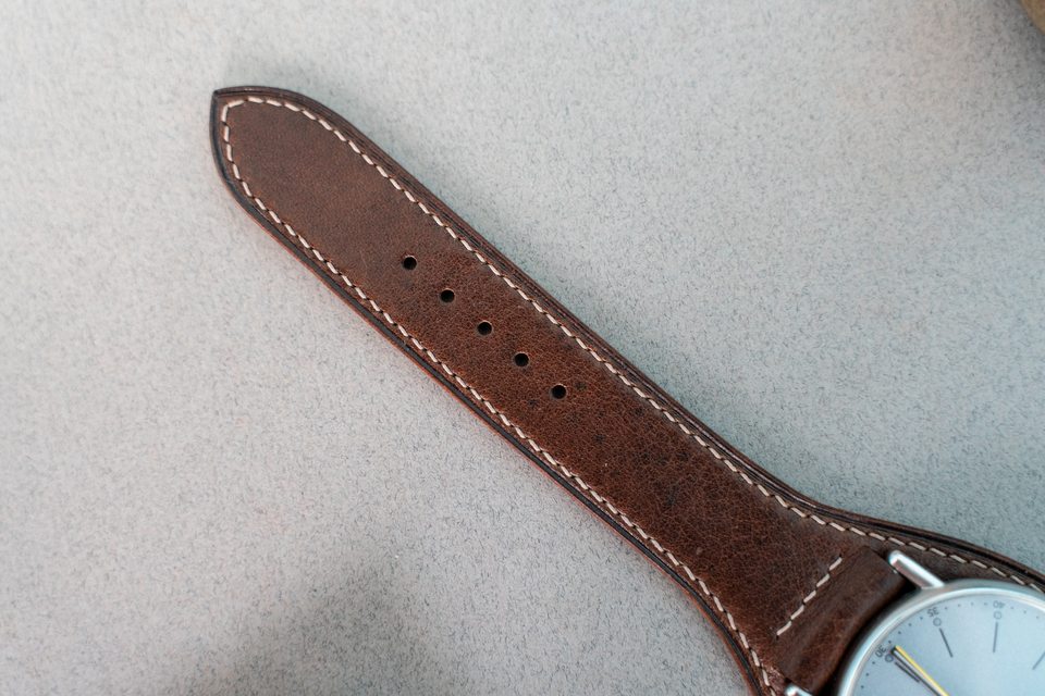 Pointed cognac strap end with adjustment holes and contrasting perimeter stitches.