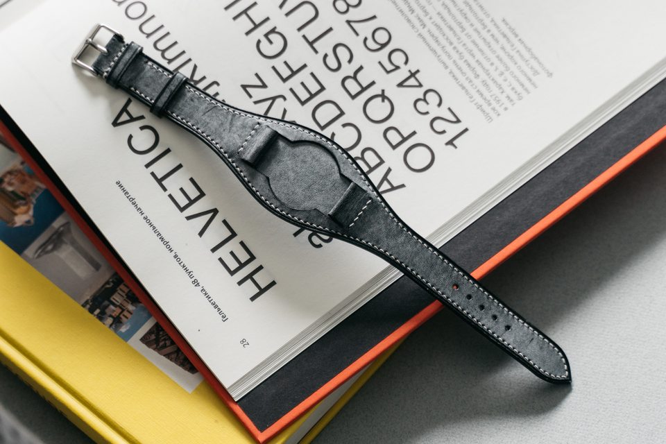 Grey Bund strap seen diagonally across an open book, with the buckle in view.