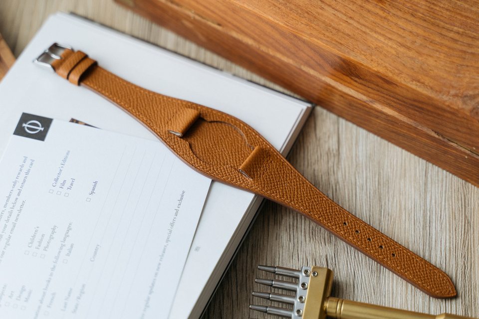Honey-coloured pebbled Bund strap laid across a book beside a stitching tool.