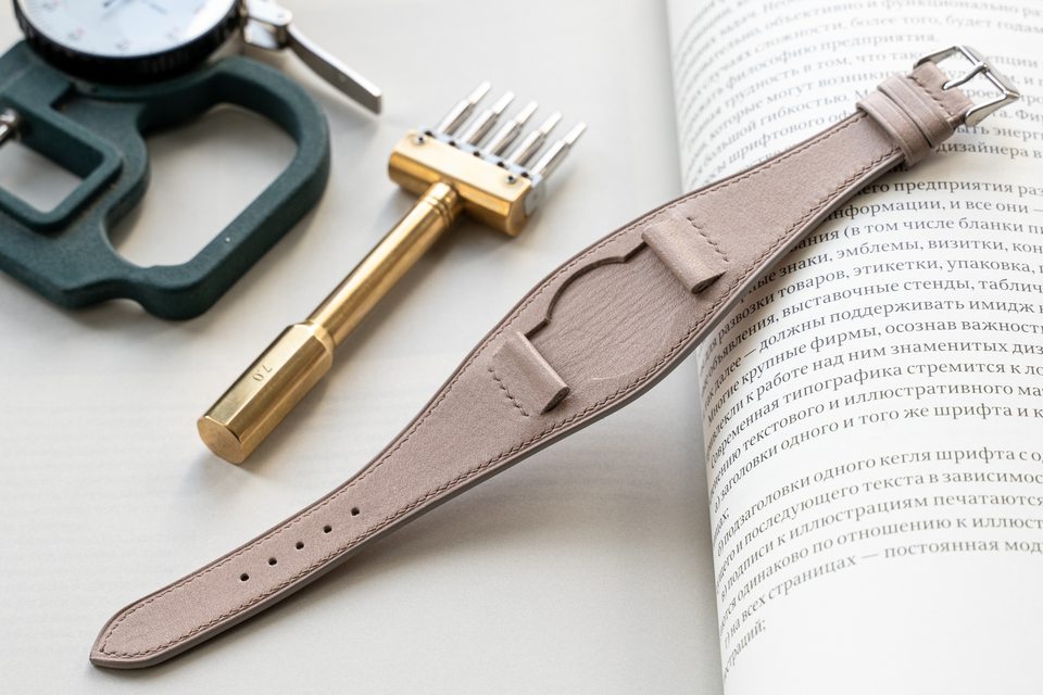 Stone-coloured Bund strap beside a stitching tool and an open book.