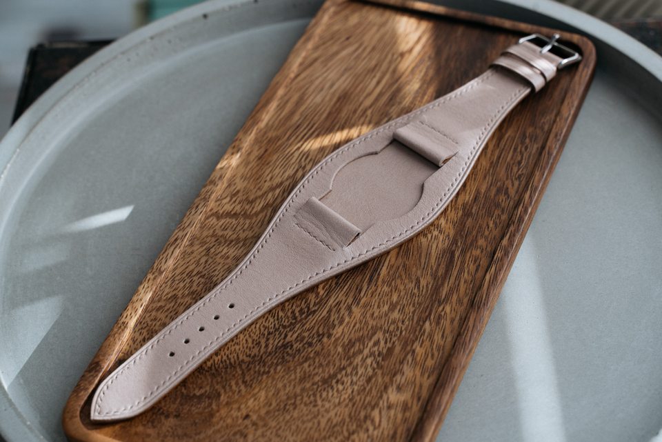 The pale stone Bund strap in side light beside the edge of a wooden tray.